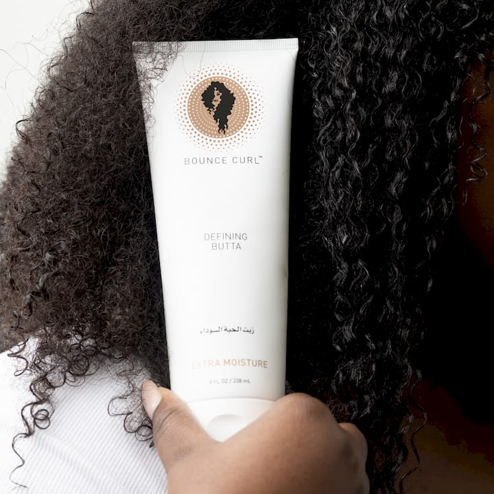 Woman applying serum to natural curly hair