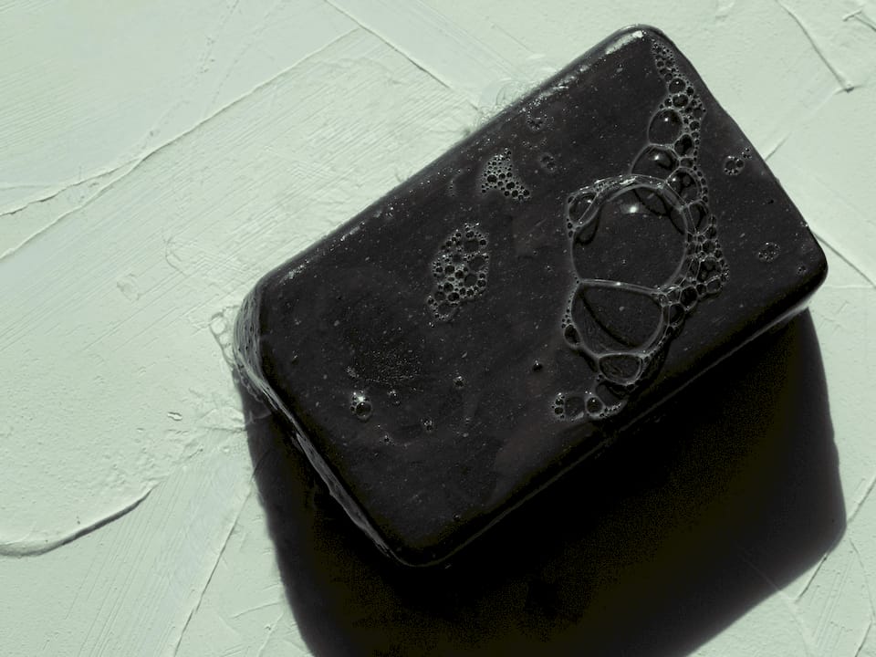 Woman applying black soap moisturizer at vanity